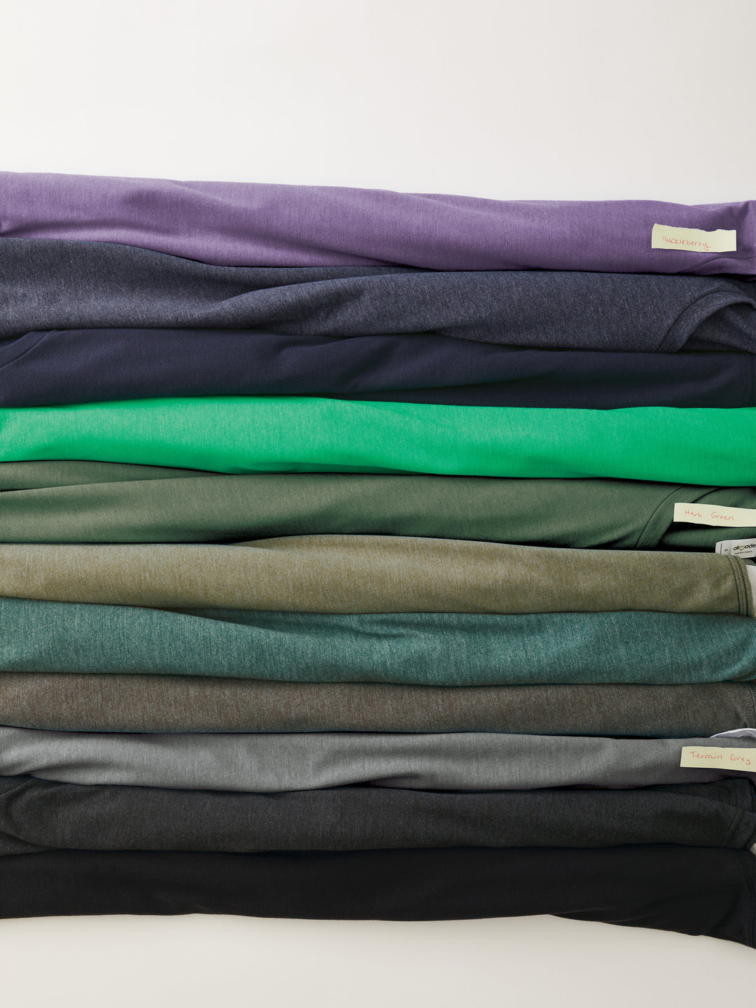 Assorted shades of Custom Allmade Tri-Blend Tees neatly folded. Sustainable and stylish, ideal for custom branding.
