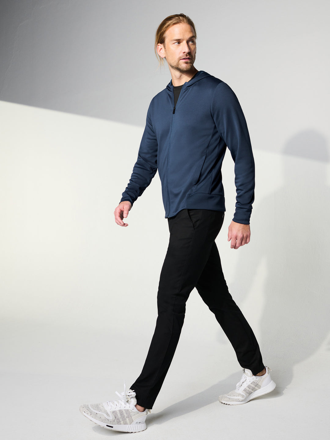 Model wearing the Custom Mercer and Mettle Double Knit Zip Hoodie in navy blue, paired with black pants and white sneakers. A stylish and functional outfit.