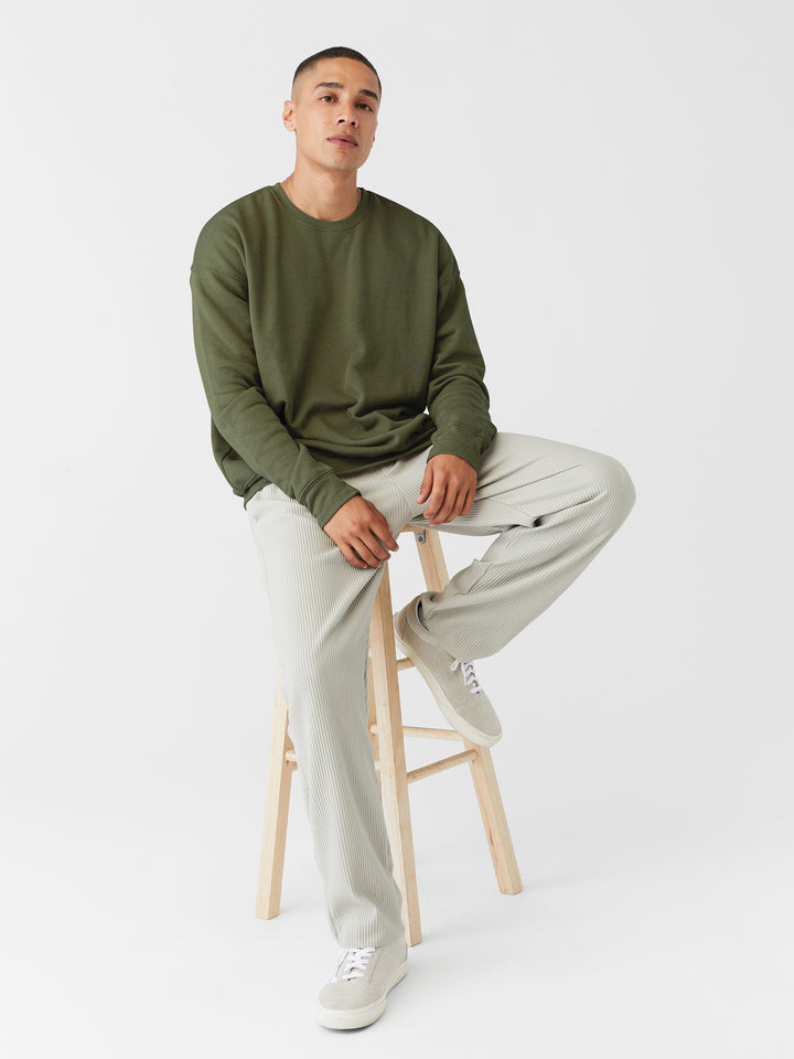 Model wearing an olive green Bella and Canvas Sponge Fleece Drop Shoulder Crewneck, styled with neutral pants for a modern look.