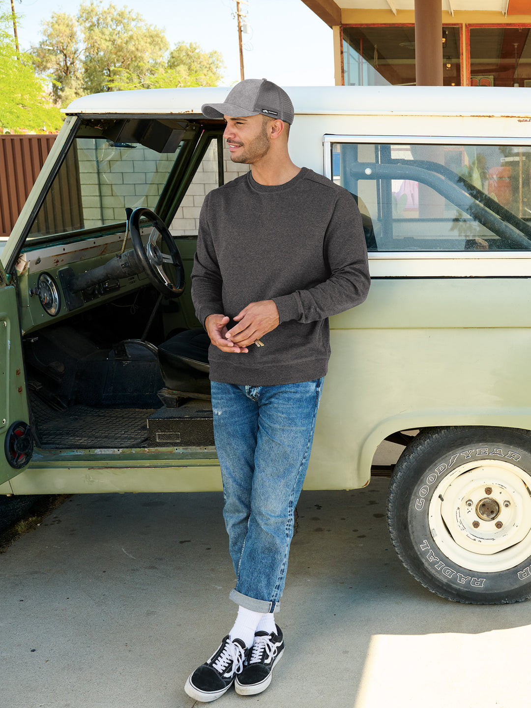 Model wearing a District Re-Fleece Custom Crewneck in dark gray, styled casually with jeans and a cap, showcasing its versatile and eco-friendly design.