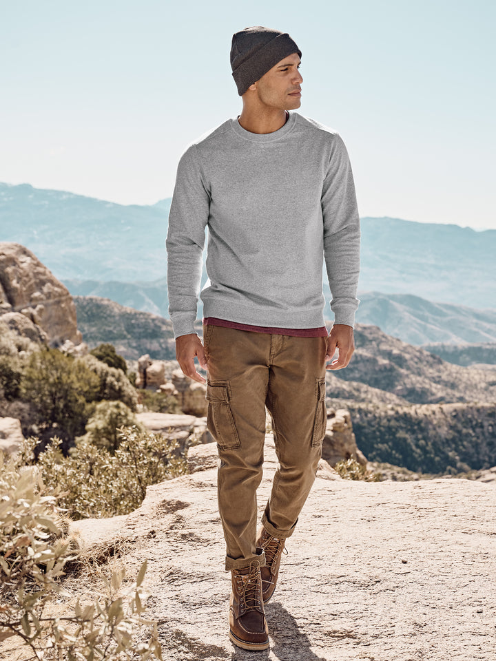 Outdoor shot of a model wearing a light gray District Re-Fleece Custom Crewneck, highlighting its sustainable fleece material in a rugged, natural setting.