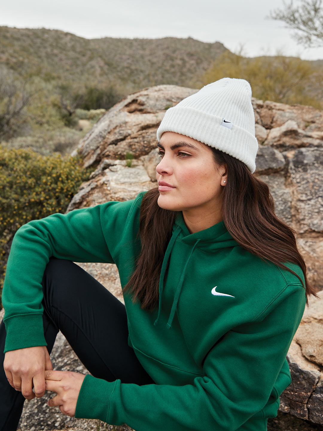 Woman outdoors wearing a white Nike Terra Beanie with a green hoodie, highlighting warmth and versatility. Ideal for custom embroidery and casual wear.