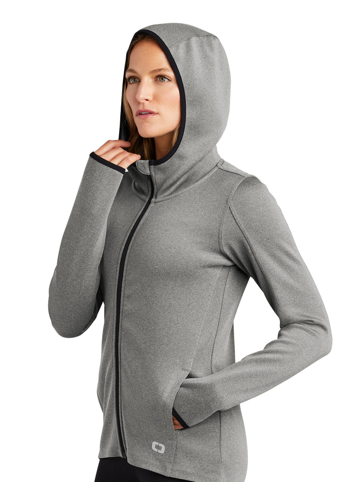 OGIO Ladies Stealth Full Zip Hooded Jacket with hood up, highlighting its streamlined design, zippered front, and thumbhole cuffs for extra warmth.