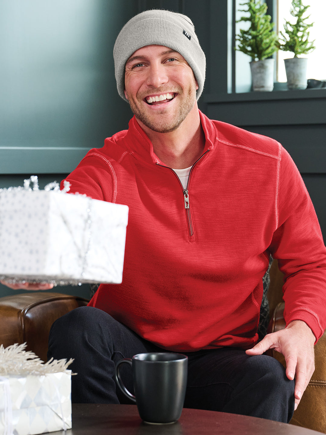 Man wearing a TravisMathew Striped Beanie in light gray, paired with a red pullover. Stylish and warm knit hat, perfect for winter and gifting occasions.